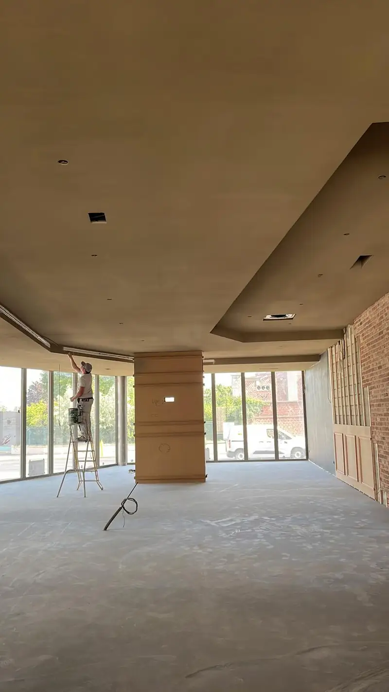 Compagnon sur escabeau finissant la retombee du plafond le long de la facade vitree, plateau de restaurant avant amenagement, mur de brique conserve apparent
