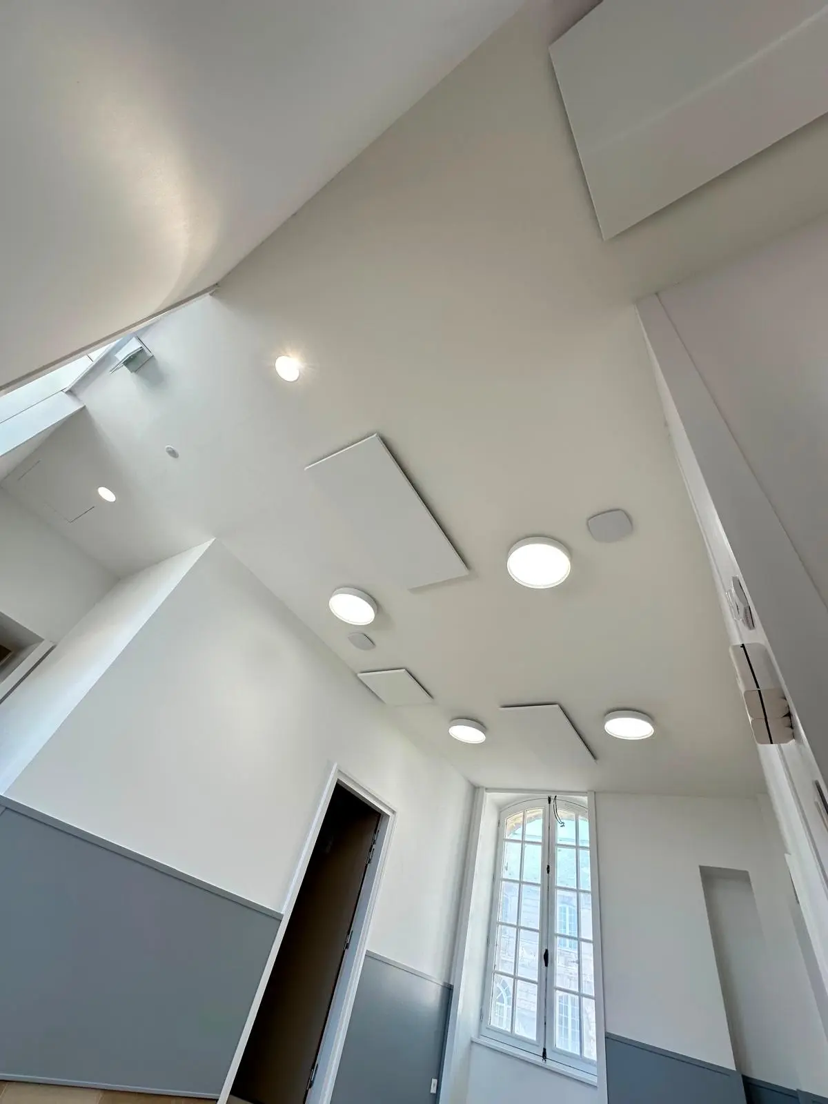 Salle claire sous plafond blanc sans joint, spots encastrés et luminaire circulaire, fenêtre à petits bois