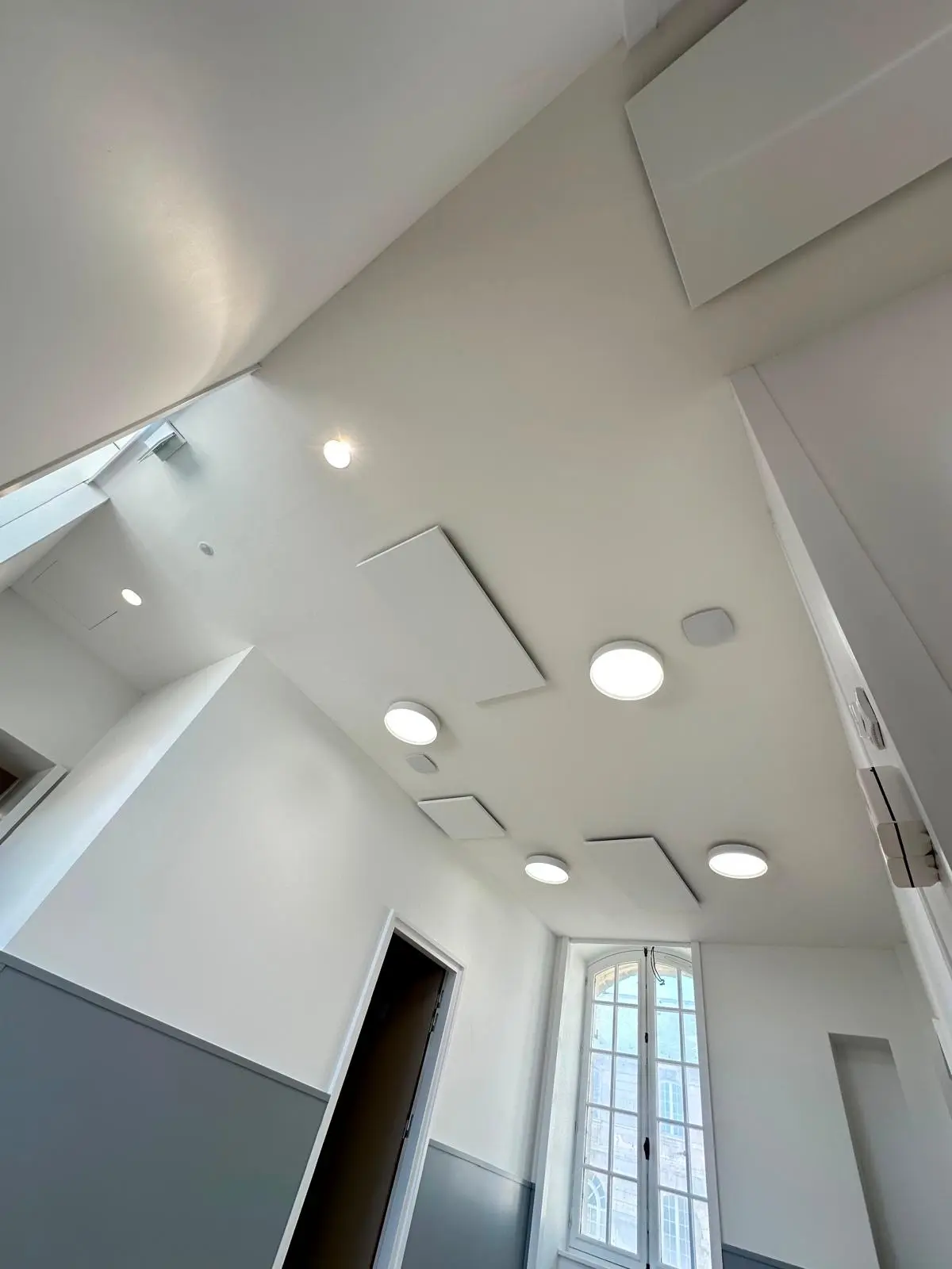 Pièce sous plafond monolithique blanc, spots et luminaire rond, embrasure de fenêtre profonde