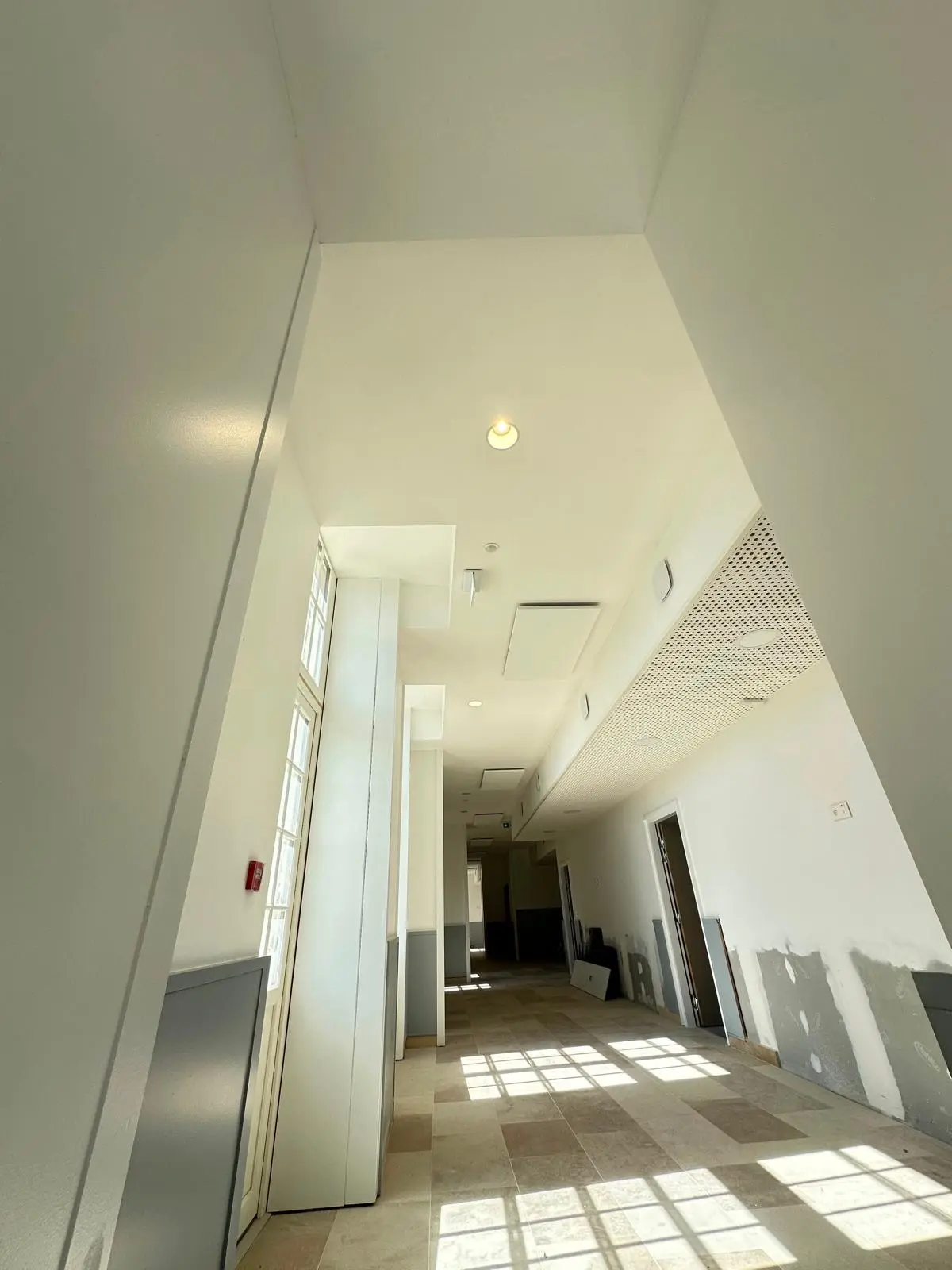 Enfilade de couloirs à plafond blanc continu, lumière naturelle au sol