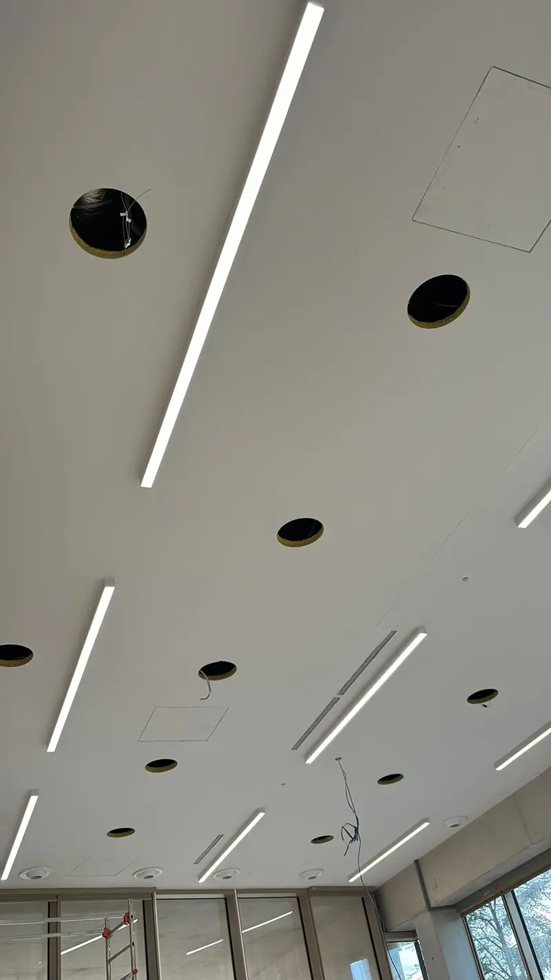 Plafond blanc rythmé de réglettes linéaires et de spots ronds encastrés