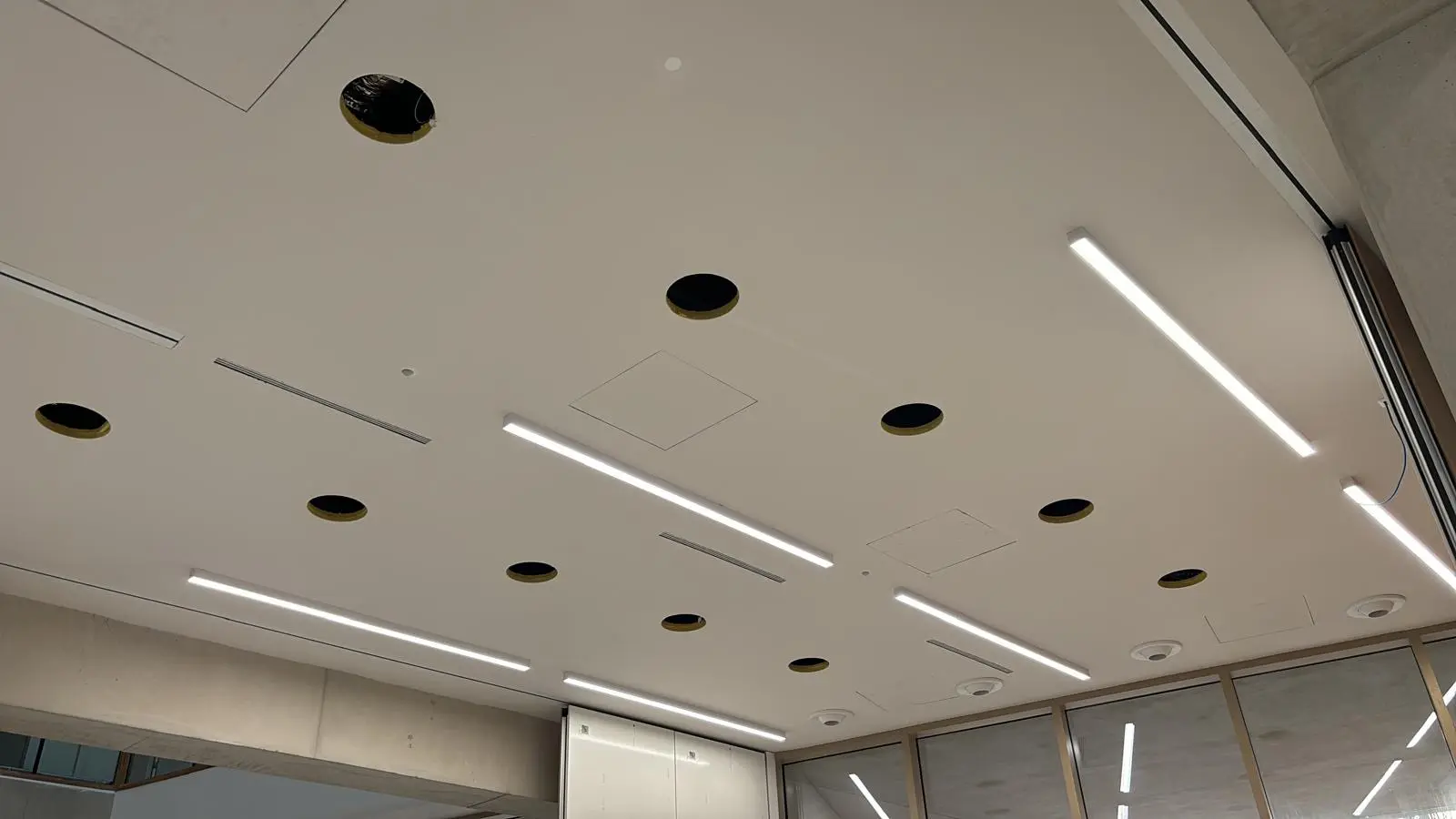 Réglettes linéaires et spots ronds intégrés dans une surface de plafond continue