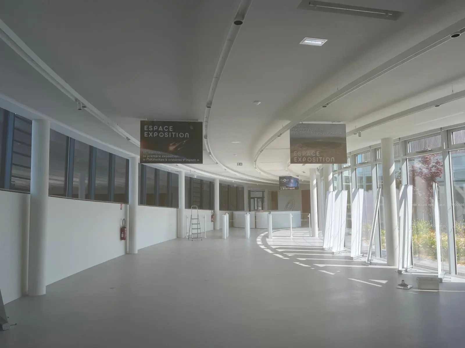 Longue galerie sous retombées courbes blanches, façade vitrée continue