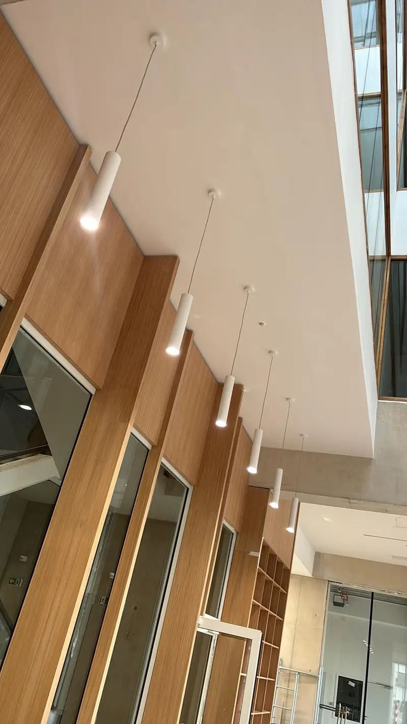 Hall habillé de bois sous plafond blanc à retombées, suspensions linéaires