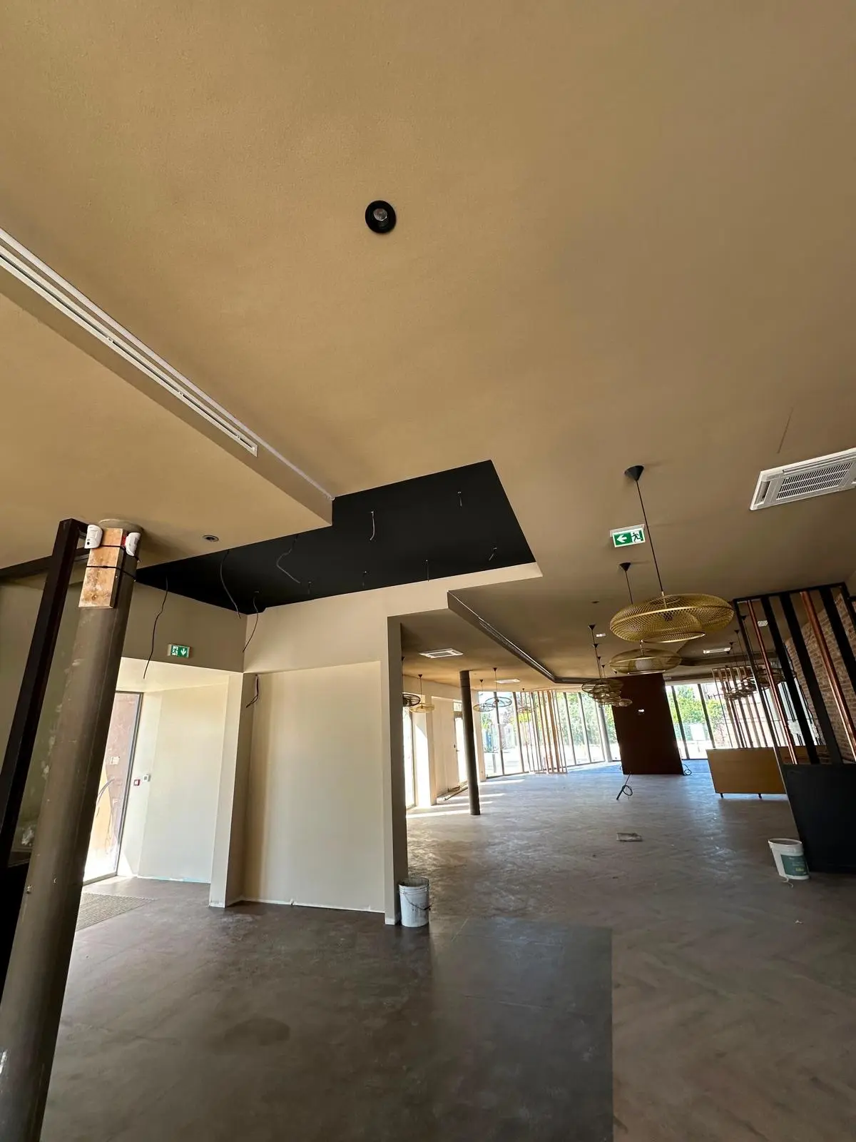 Salle sous plafond clair avec voiles techniques sombres et suspensions dorées