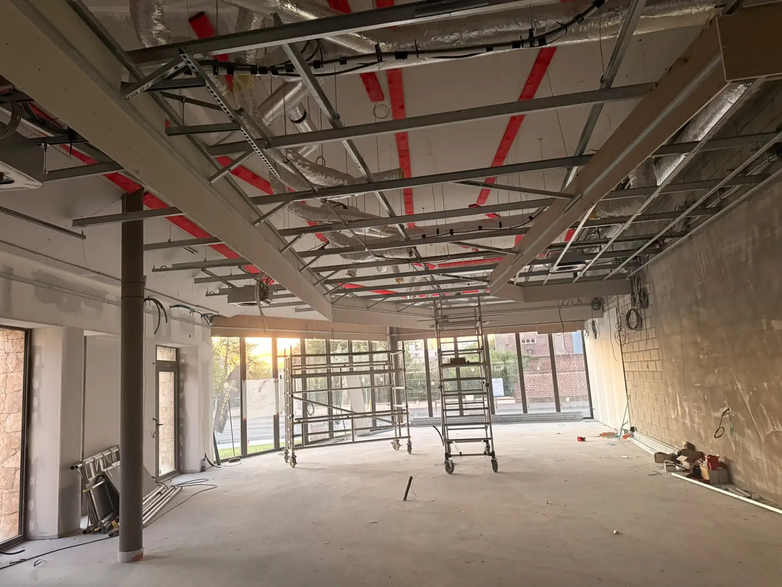 Plateau en chantier sous l'ossature métallique du plafond, suspentes réglées et bandes de repérage, échafaudage roulant devant la façade vitrée