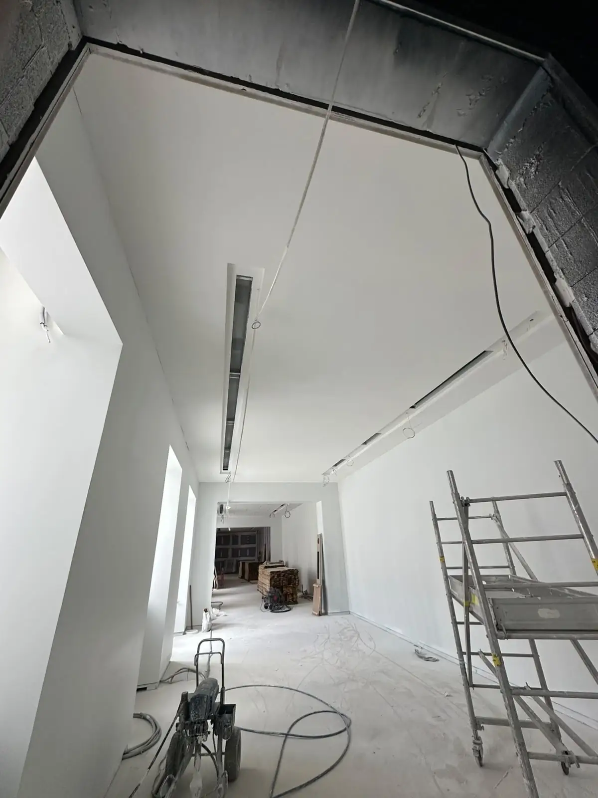 Retombée de plafond terminée le long d'une circulation, plénum encore ouvert au-dessus, échafaudage roulant en place