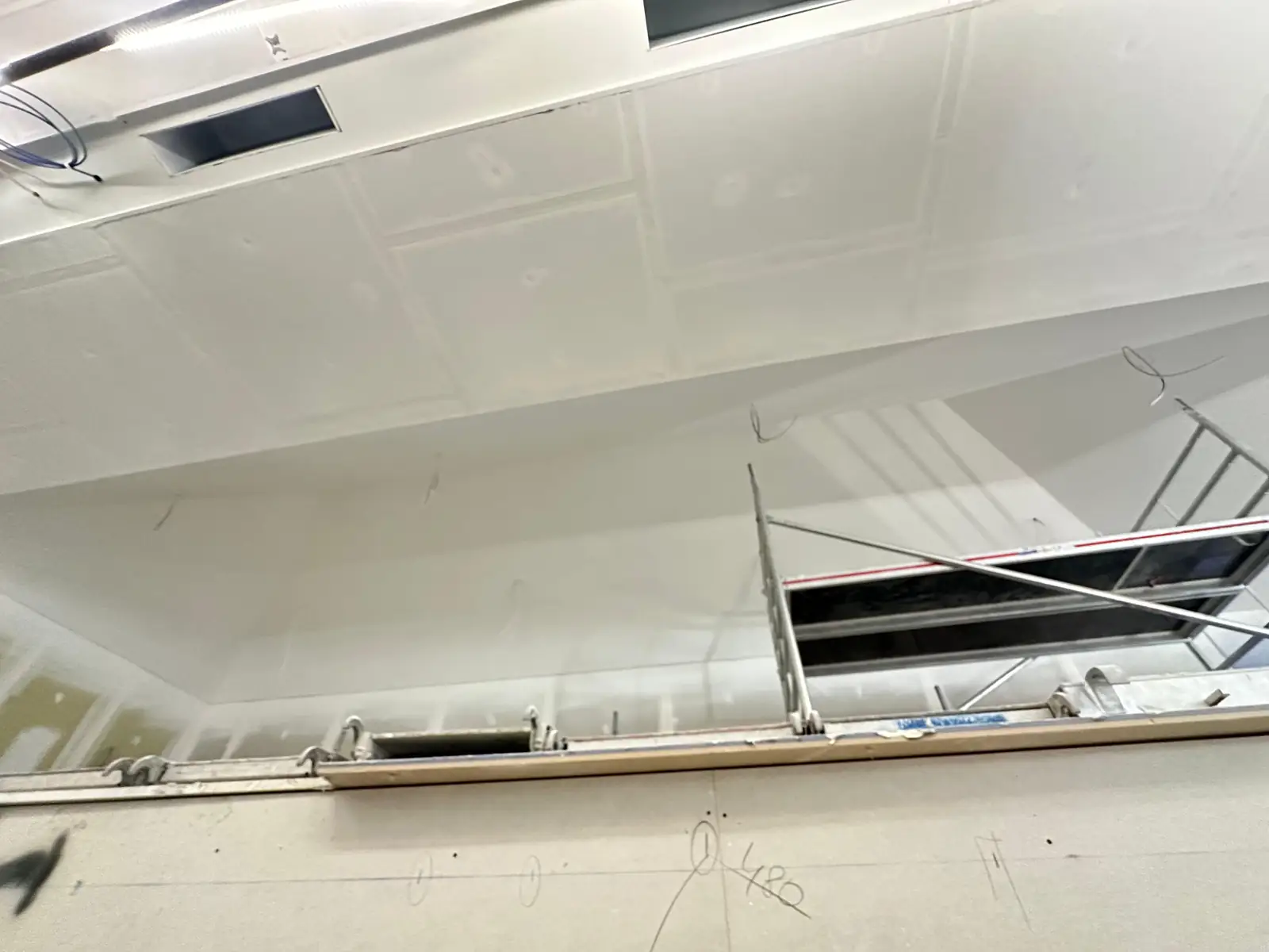 Plafond plaqué et bandé sur toute la longueur d'un plateau, bouches de ventilation et luminaires linéaires encastrés, échafaudage roulant sous une réservation encore ouverte