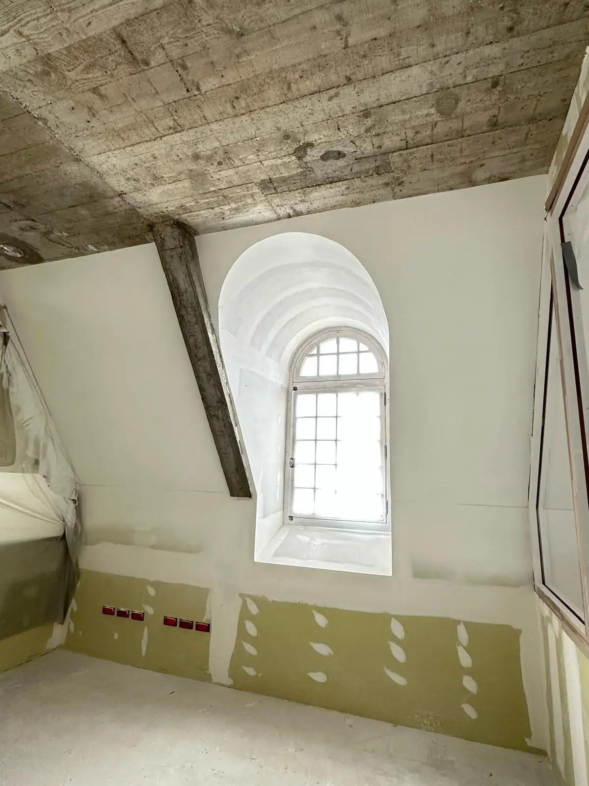 Lucarne à ébrasement cintré en plâtre lissé sous une dalle de béton coffrée en planches, bas de cloison en plaque avant enduit, boîtiers électriques posés