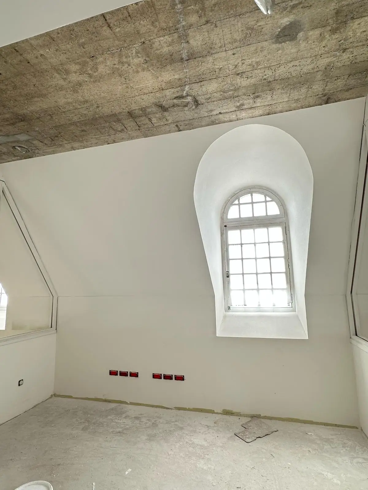 Lucarne cintrée terminée : ébrasement galbé en plâtre lissé raccordé au mur plan sans rupture, boîtiers électriques alignés en attente