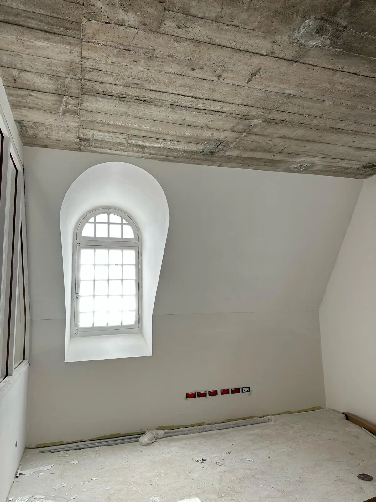Lucarne cintrée vue de face, ébrasement lissé au plâtre en forme de goutte, dalle de béton coffrée conservée apparente au plafond