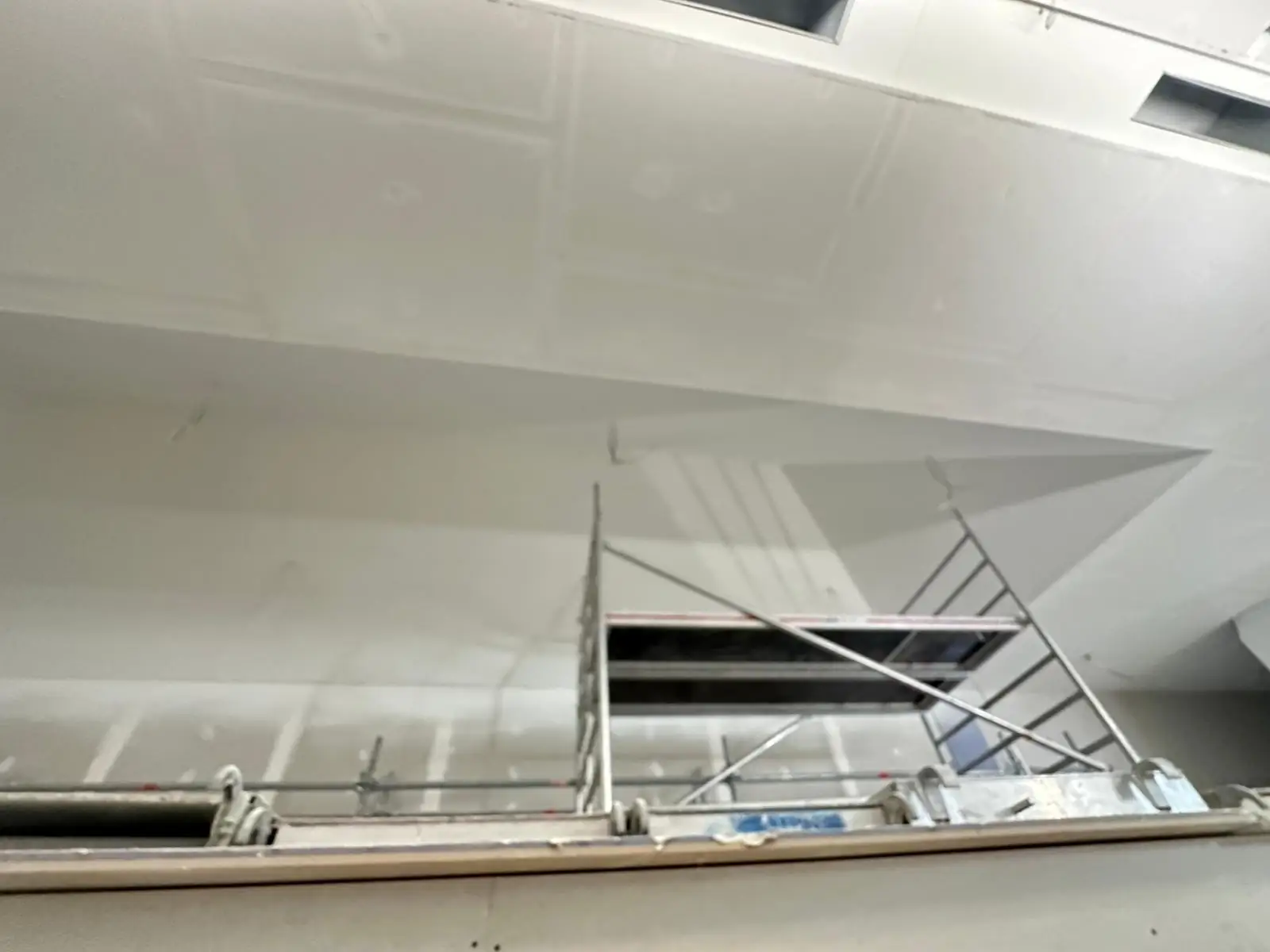 Plafond plaqué et bandé le long d'une retombée droite, échafaudage roulant sous une réservation de plafond encore ouverte