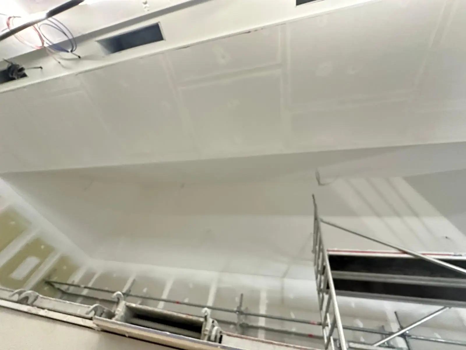 Plafond plaqué et joints enduits le long d'une retombée, bouches de ventilation encastrées, échafaudage roulant en place