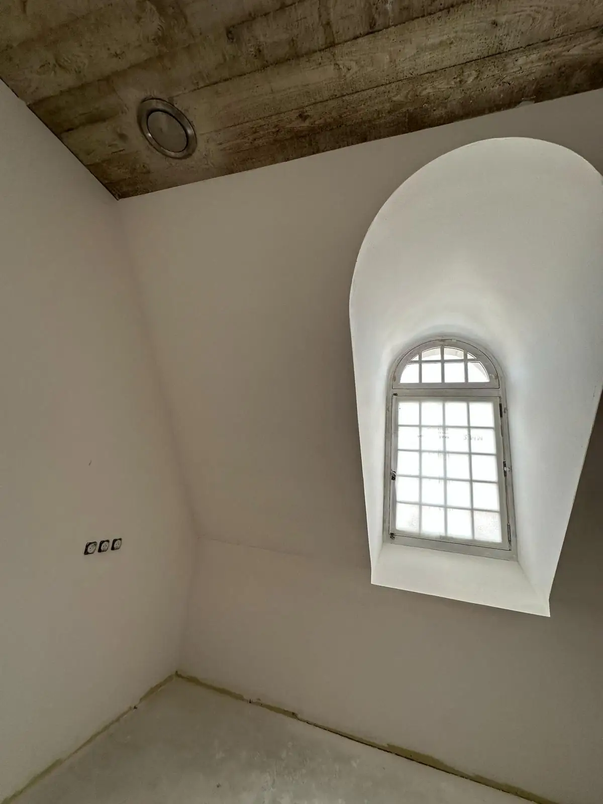 Lucarne à ébrasement cintré lissé au plâtre sous la dalle de béton coffrée, oculus de ventilation encastré dans la retombée