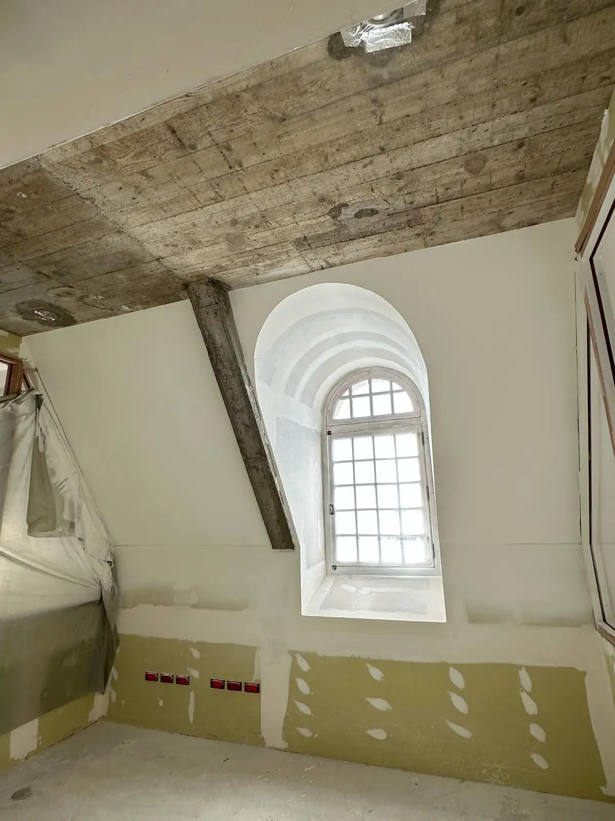 Combles en fin de chantier : lucarne cintrée terminée, poutre et dalle coffrée conservées apparentes, bas de cloison encore en plaque