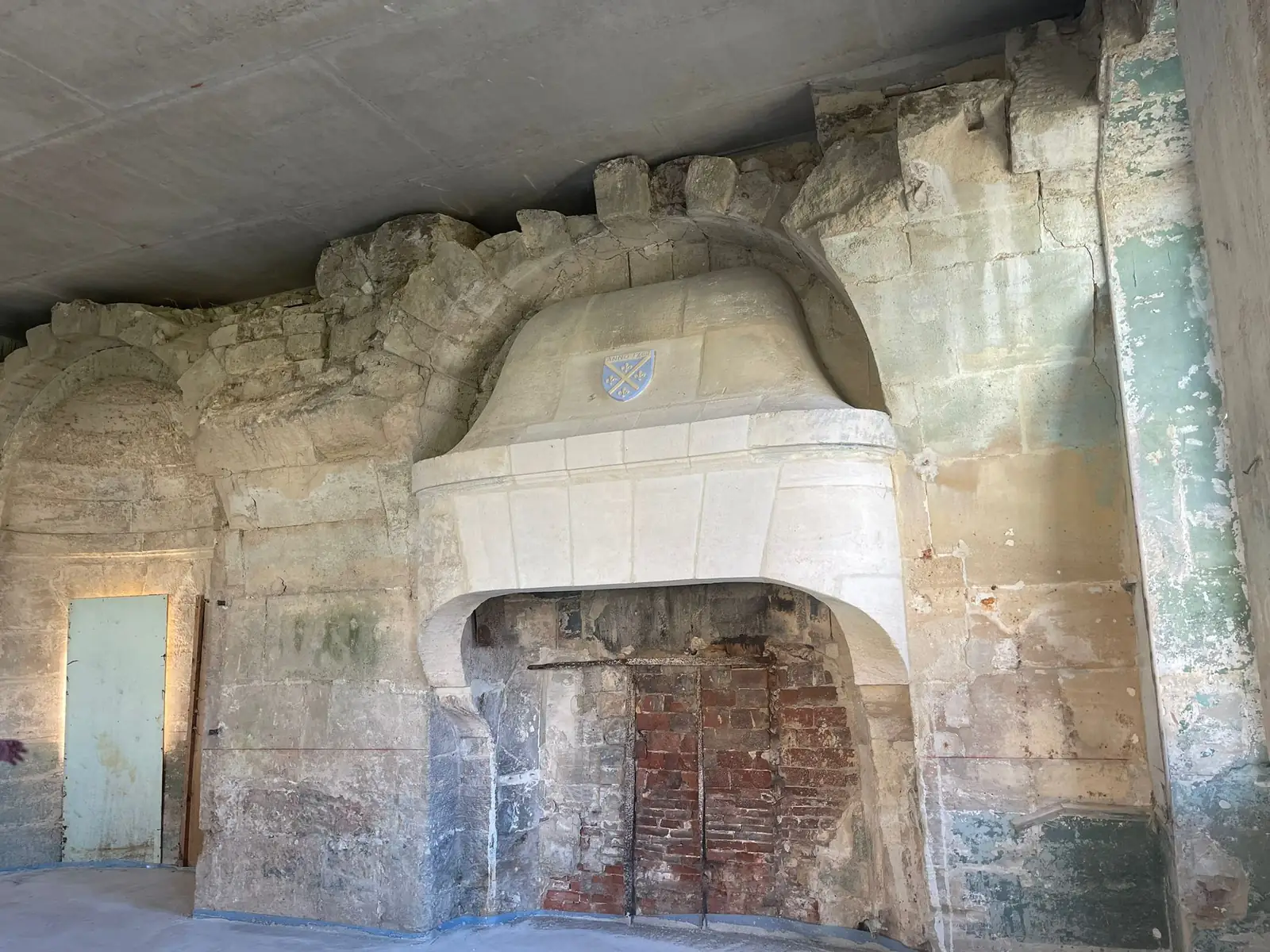 Cheminée de pierre à cartouche armorié avant travaux, foyer de brique apparent et enduits piquetés