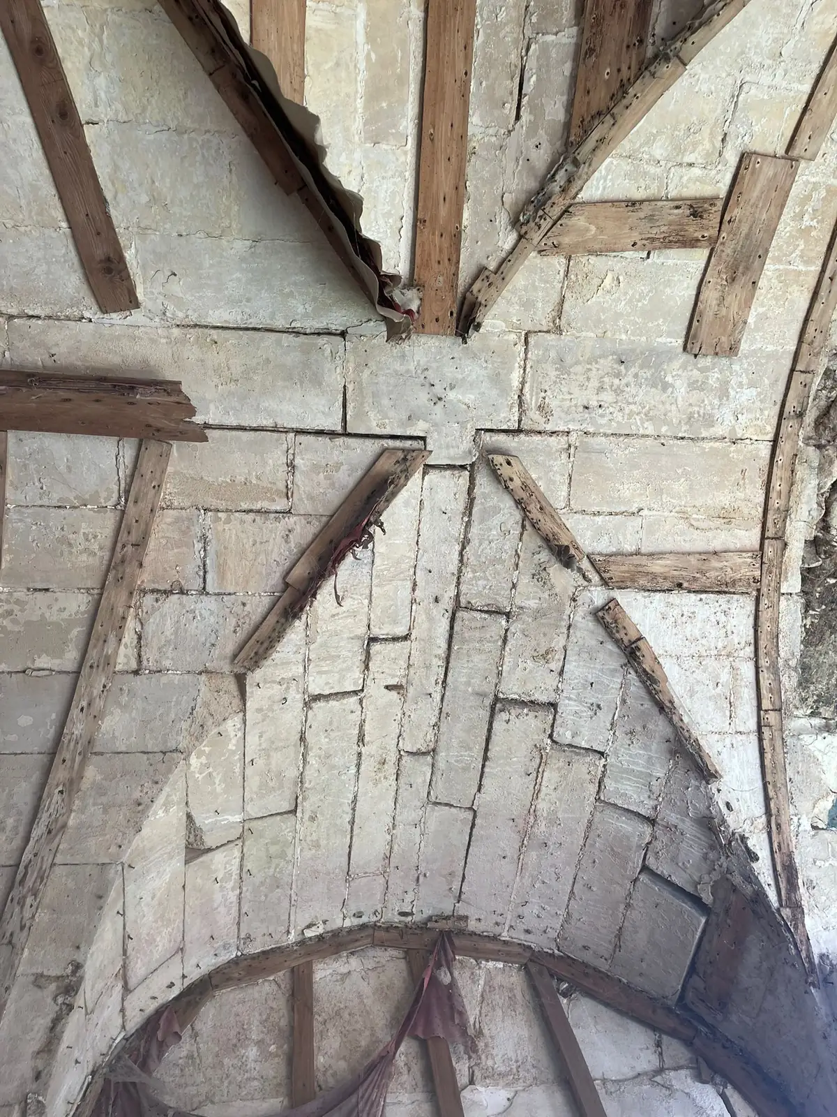 Assemblage de charpente ancienne en étoile au sommet d'une voûte de pierre, avant travaux