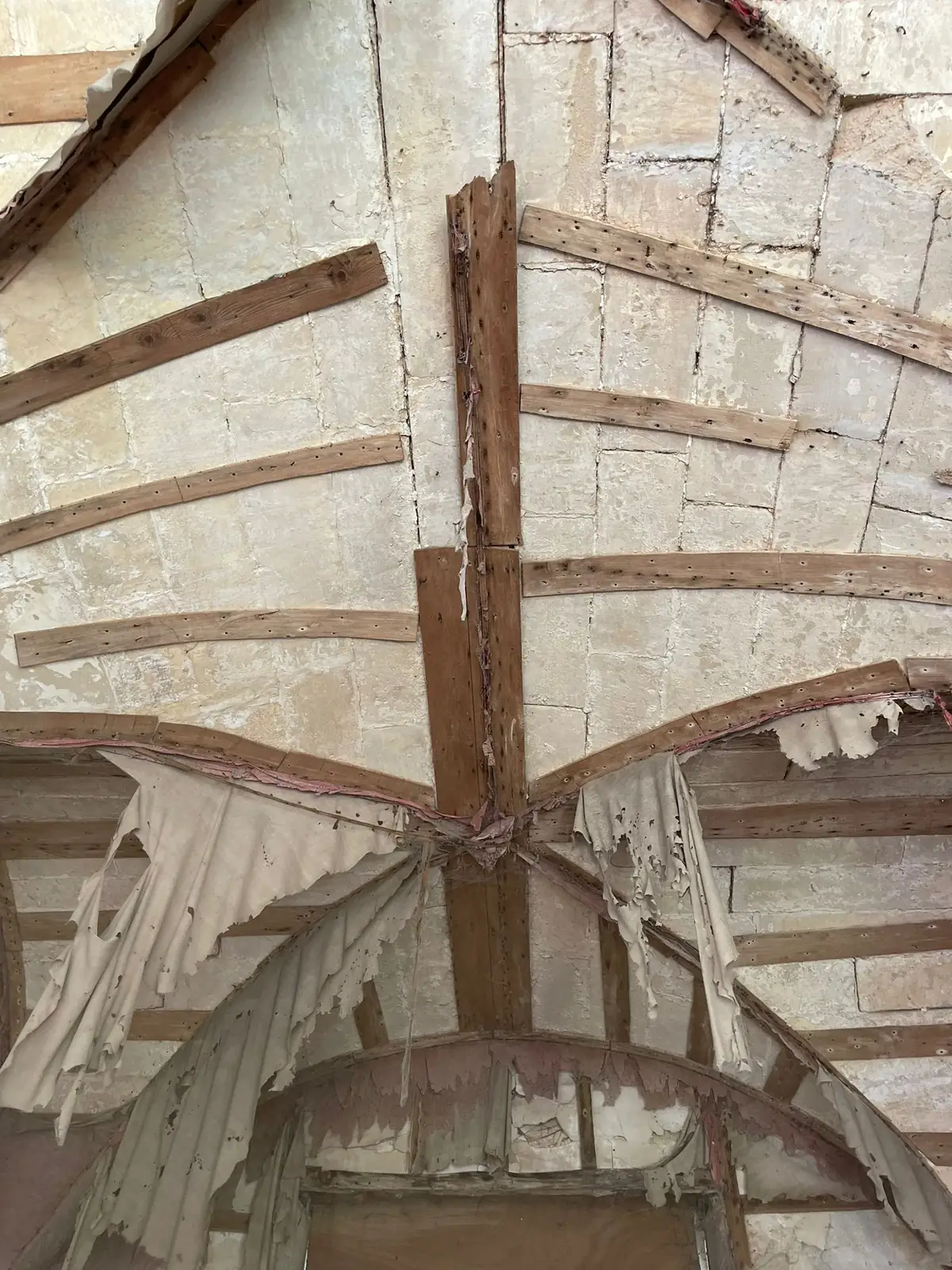 Charpente ancienne au-dessus d'une voûte de pierre, pièces de bois assemblées en étoile, avant travaux