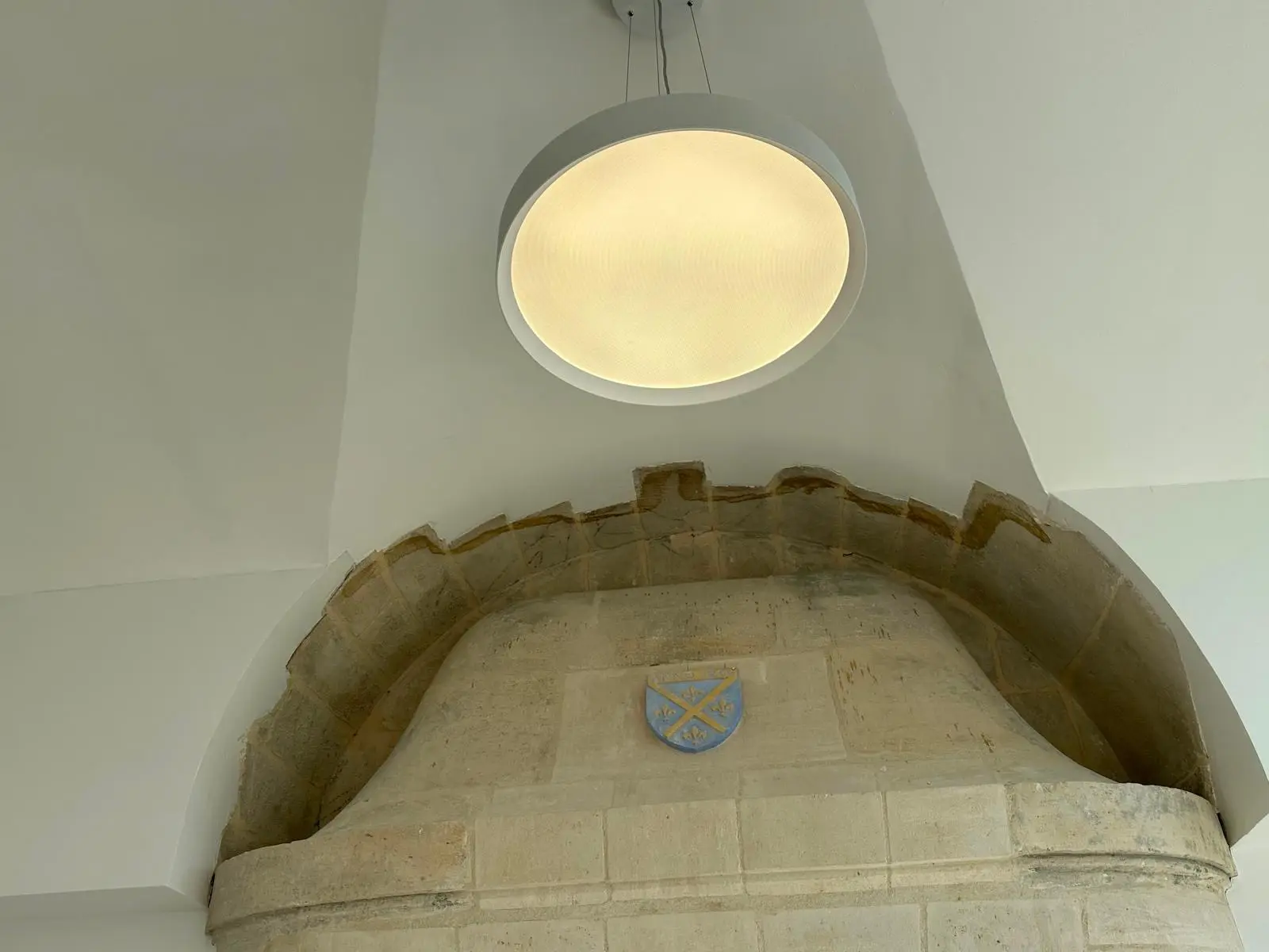 Voûte blanche monolithique se refermant autour d'un arc de pierre apparent, luminaire circulaire encastré