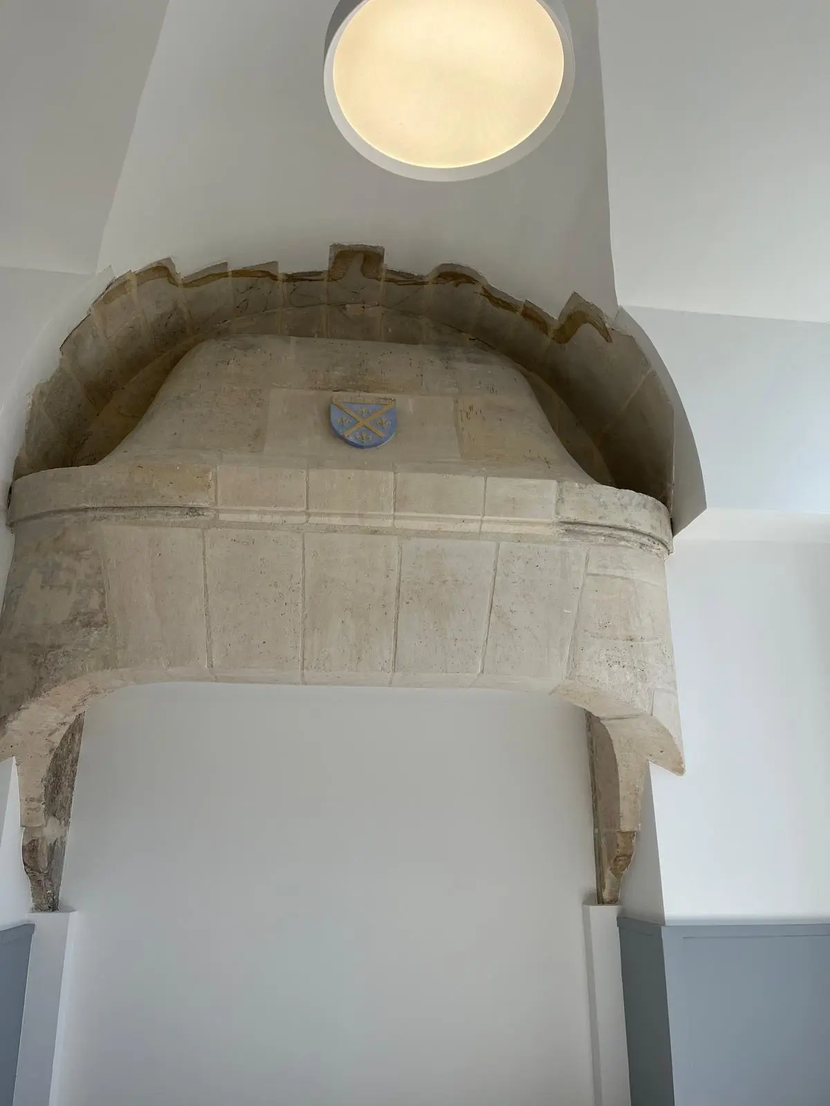Arc de pierre conservé sous une voûte plâtre lisse, oculus lumineux encastré au sommet
