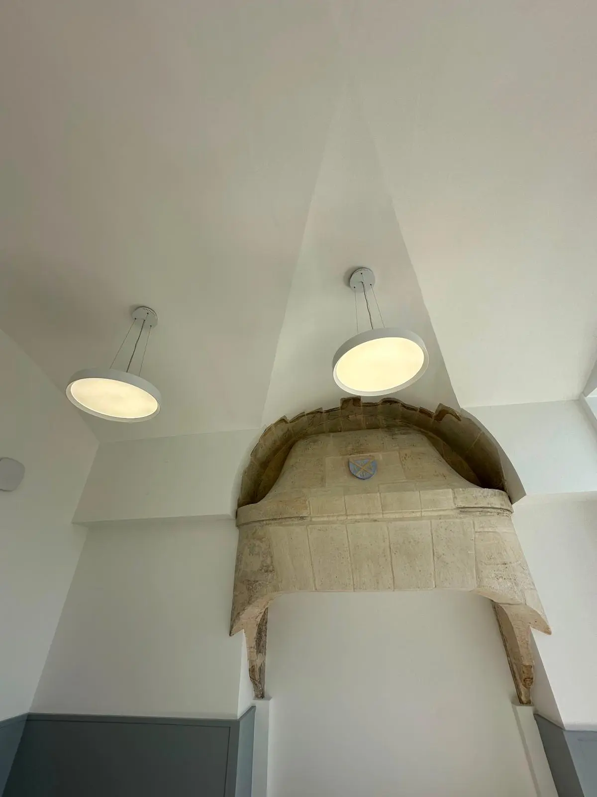 Deux luminaires ronds affleurants dans une voûte blanche continue au-dessus d'un arc en pierre