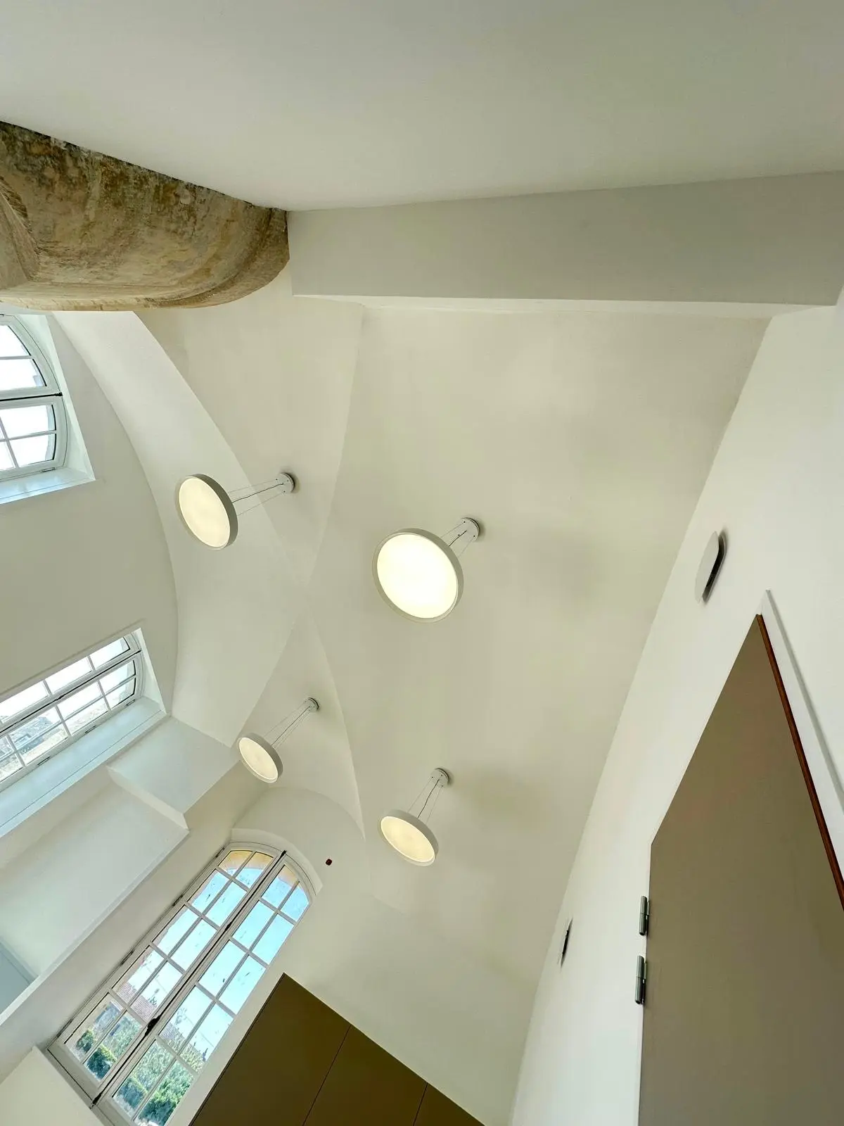 Voûte blanche percée d'un oculus lumineux et de spots ronds, arc de pierre en partie haute
